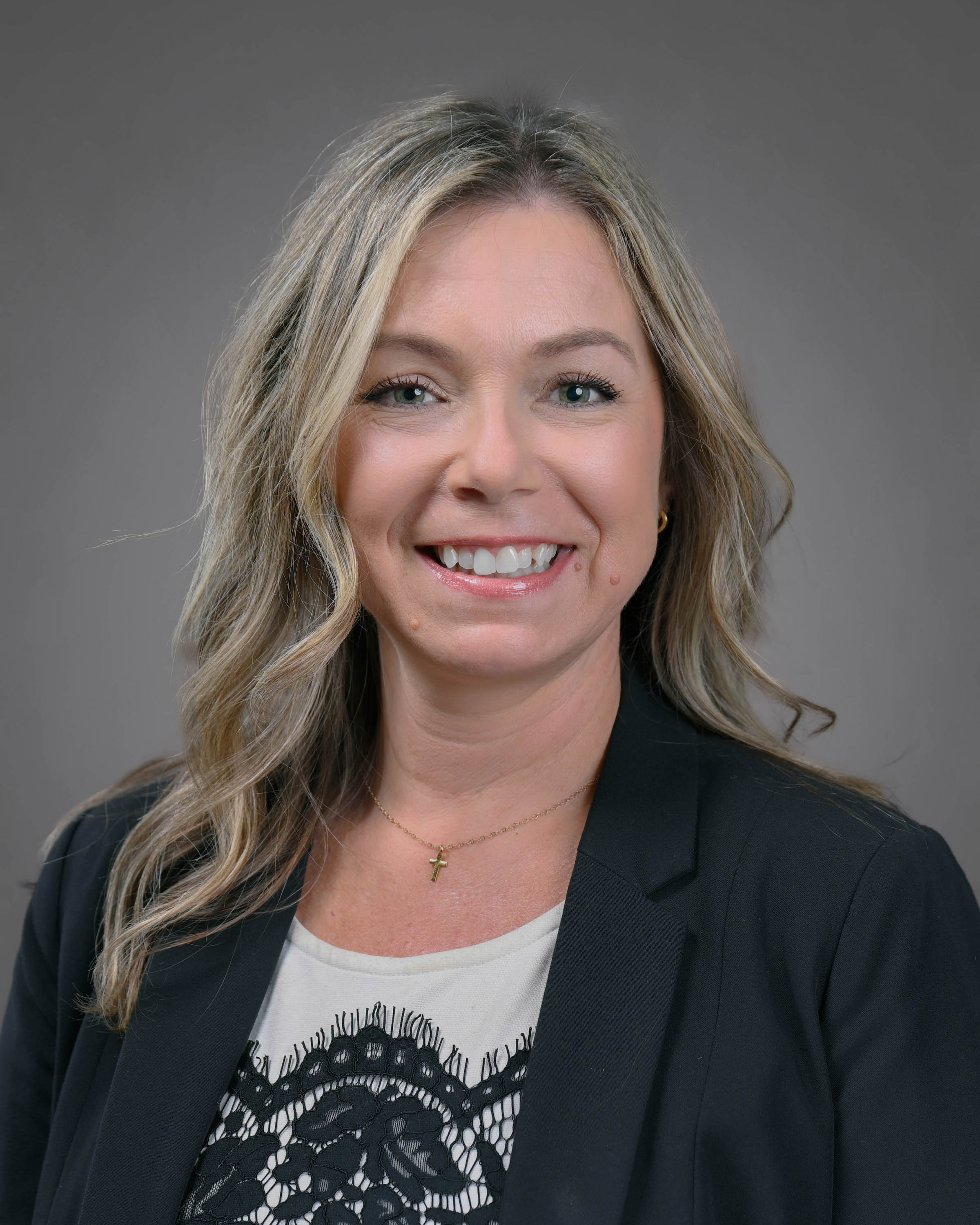 Kind looking woman smiling with blonde and brown hair in a dark jacket with a white and black shirt.